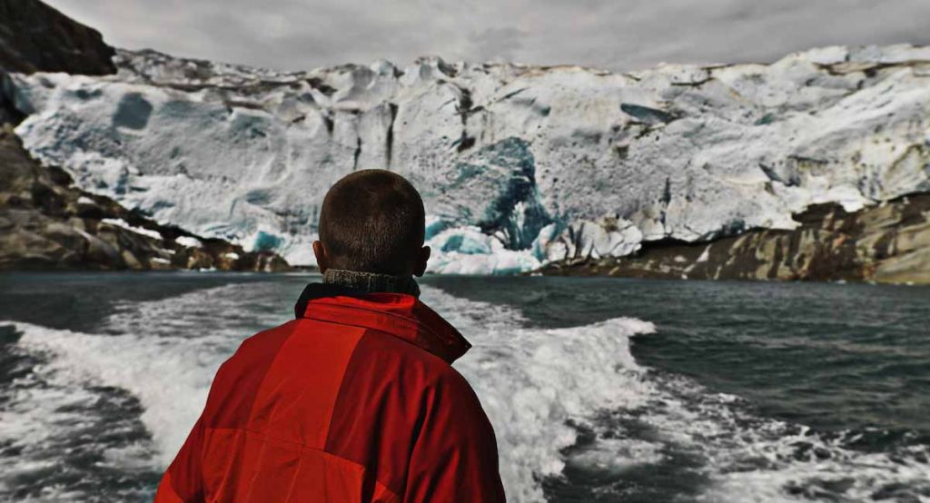 a_traveller_in_red_clothes_staring_at_the_glacier_from_a_boat